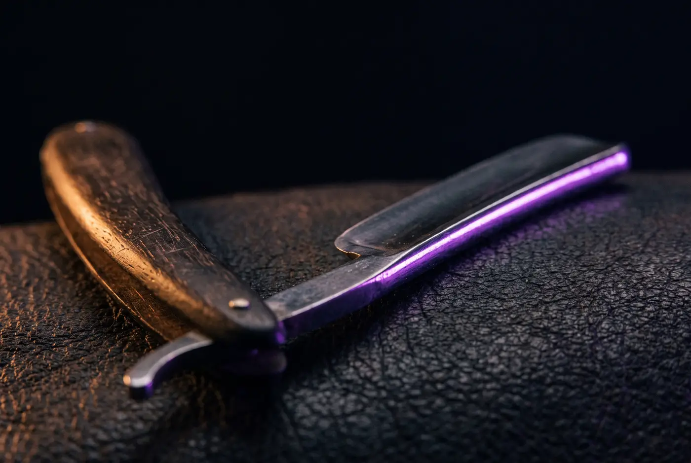 Navalha clássica sobre couro escuro, com reflexo neon violeta no fio da lâmina